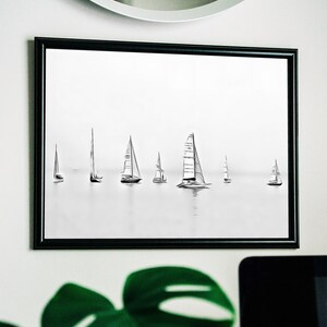 K&ouml;nnte beinhalten: Ein schwarz-wei&szlig; gerahmter Druck einer minimalistischen Zeichnung von Segelbooten auf dem Wasser. Die Segelboote sind unterschiedlich gro&szlig; und in einer Reihe angeordnet.