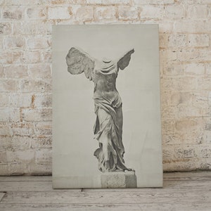 May include: A black and white print of the statue of the Winged Victory of Samothrace, also known as Nike of Samothrace. The statue is a Greek sculpture from the Hellenistic period, depicting the goddess Nike, the goddess of victory, landing on the prow of a ship.
