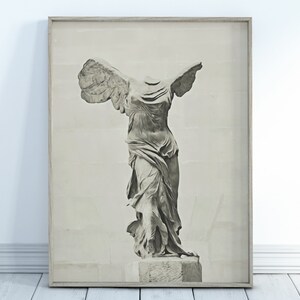May include: A black and white photograph of the Winged Victory of Samothrace statue, a famous ancient Greek sculpture. The statue is displayed in a frame.