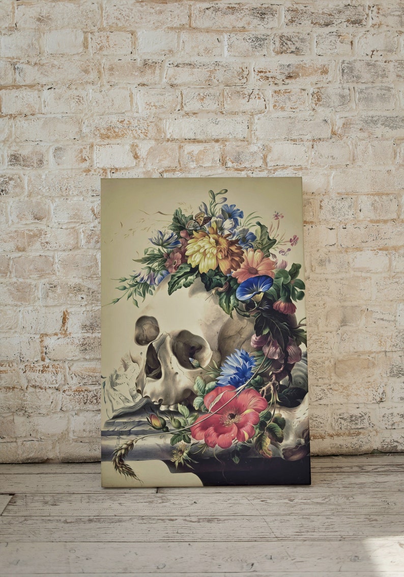 May include: A vintage still life print featuring a human skull adorned with a colorful floral arrangement. The skull is surrounded by various flowers, including red, pink, blue, and yellow blooms. The artwork is set against a light beige background.