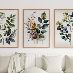 May include: Three framed watercolor paintings of leafy branches with green, blue, and yellow leaves. The paintings are in wooden frames and are hung on a white wall.