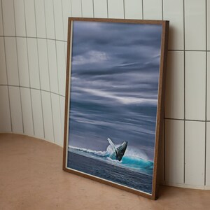 May include: A framed print featuring a breaching whale in a turbulent ocean scene under a dramatic, cloudy sky. The artwork is encased in a brown wooden frame, adding a touch of warmth to the cool tones of the ocean and sky.