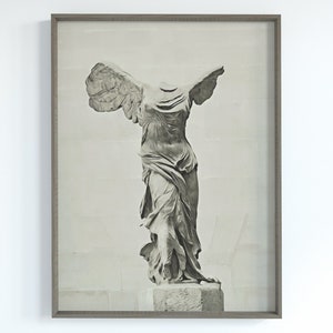 May include: A black and white photograph of the Winged Victory of Samothrace statue, a famous ancient Greek sculpture, displayed in a grey frame.