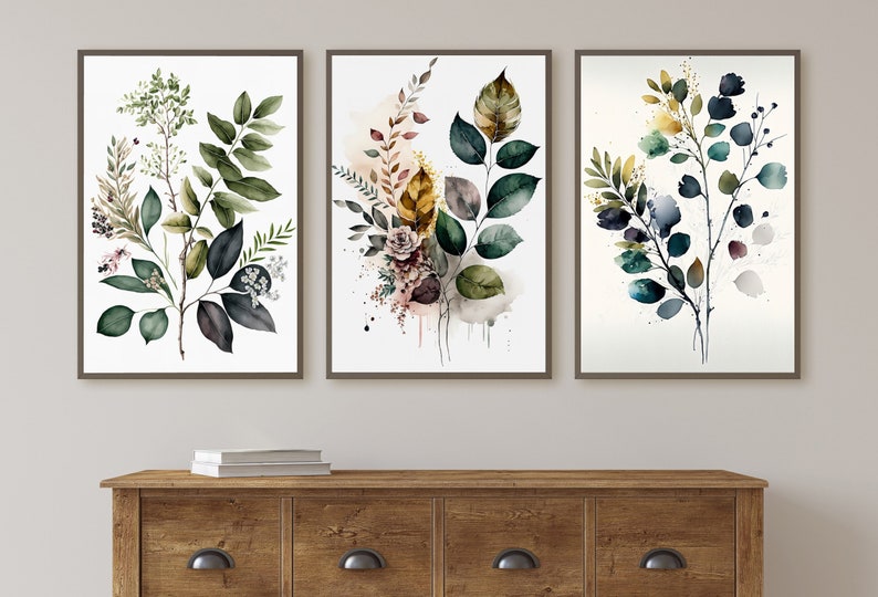 May include: Three framed watercolor prints featuring botanical illustrations of leaves and branches in shades of green, blue, and brown. The prints are arranged in a row on a wall.