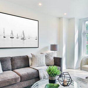 K&ouml;nnte beinhalten: Ein Wohnzimmer mit einem grauen Sofa, einem wei&szlig;en Sessel, einem schwarz gerahmten Bild von Segelbooten, einem Glas-Couchtisch und einer Topfpflanze.