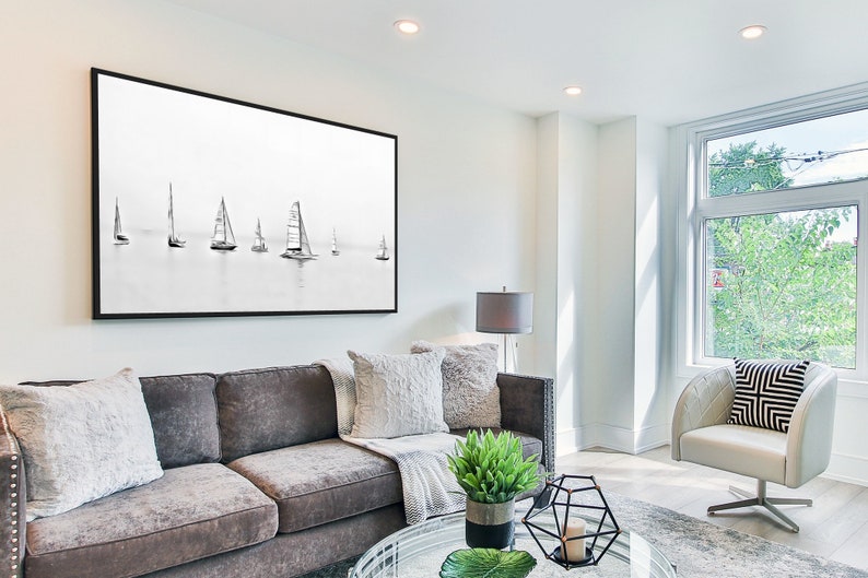 K&ouml;nnte beinhalten: Ein Wohnzimmer mit einem grauen Sofa, einem wei&szlig;en Sessel, einem schwarz gerahmten Bild von Segelbooten, einem Glas-Couchtisch und einer Topfpflanze.