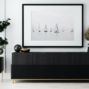 K&ouml;nnte beinhalten: Ein schwarzes und goldenes Sideboard mit drei T&uuml;ren und einem unteren Regal. Das Sideboard hat ein schlankes, modernes Design und ist mit einem Schwarzwei&szlig;foto von Segelbooten auf dem Wasser dekoriert.