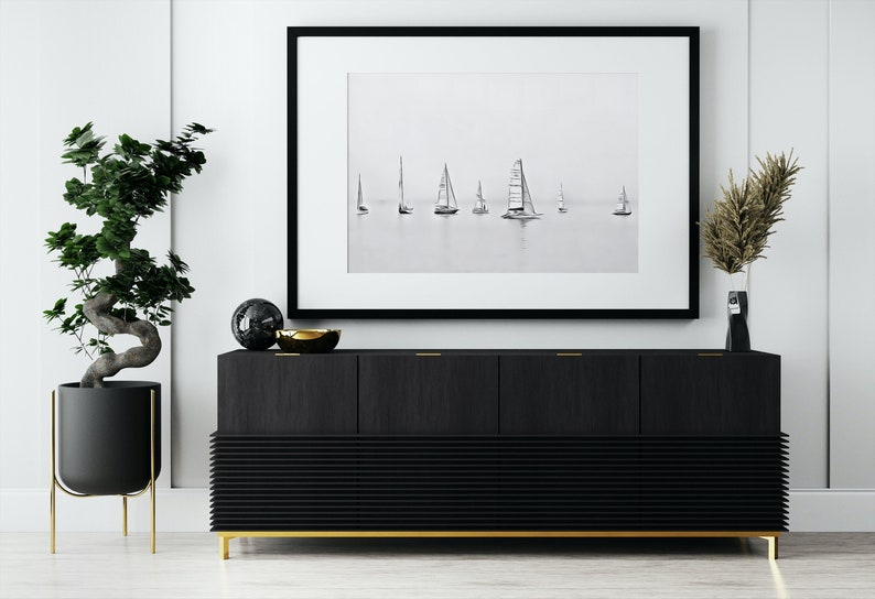 K&ouml;nnte beinhalten: Ein schwarzes und goldenes Sideboard mit drei T&uuml;ren und einem unteren Regal. Das Sideboard hat ein schlankes, modernes Design und ist mit einem Schwarzwei&szlig;foto von Segelbooten auf dem Wasser dekoriert.