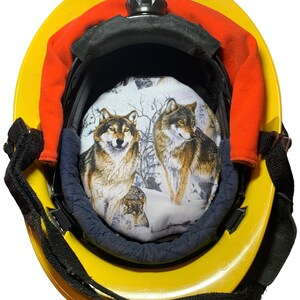May include: Yellow hard hat with a black interior and a padded liner featuring a wolf design. The liner shows two wolves in a snowy forest scene. The hat has a black adjustable strap and orange padding.