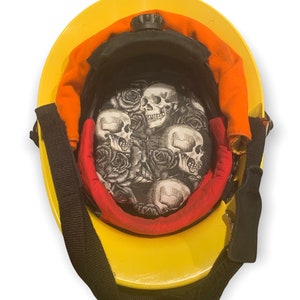 May include: Yellow firefighter helmet with a black skull and rose pattern liner. The helmet has a black strap and a red and orange liner.