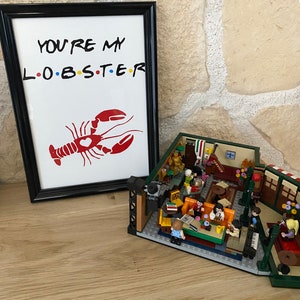 May include: A framed print with the text "YOU'RE MY L.O.B.S.T.E.R" and a red lobster illustration. Beside it is a Lego set depicting a cafe scene with miniature figures and furniture.