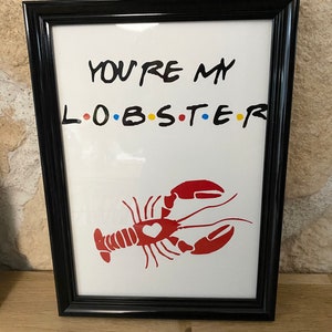 May include: A framed print with the text "YOU'RE MY L.O.B.S.T.E.R" in black, with the letters "O.B.S.T.E.R" in the colors red, yellow, blue, and a red lobster illustration with a heart. The frame is black.
