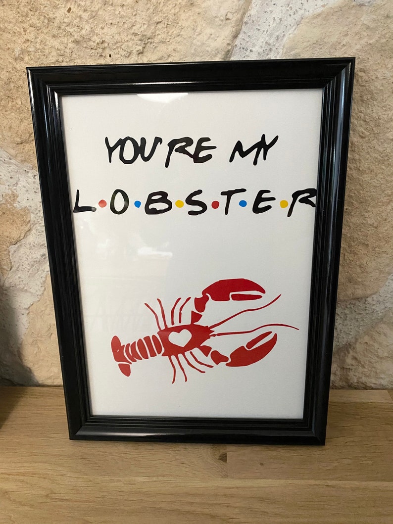 May include: A framed print with the text "YOU'RE MY L.O.B.S.T.E.R" in black, with the letters "O.B.S.T.E.R" in the colors red, yellow, blue, and a red lobster illustration with a heart. The frame is black.