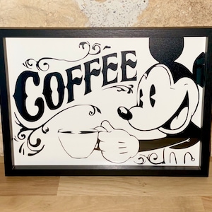 Peut inclure: Impression encadrée en noir et blanc représentant Mickey Mouse tenant une tasse de café avec le mot "COFFEE" dans une police vintage.