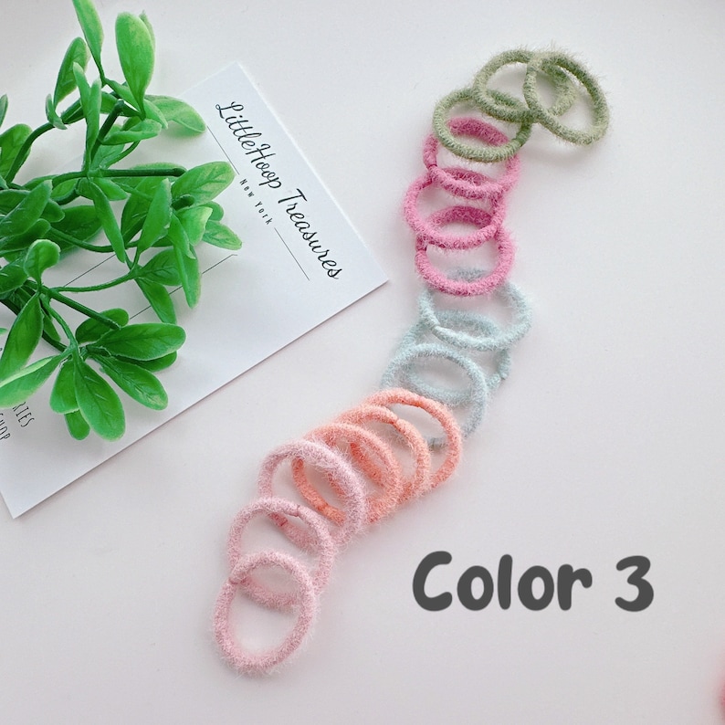 Puede incluir: Un conjunto de 10 gomas para el pelo de color borroso en tonos de rosa, melocot&oacute;n, azul claro y verde. Las gomas para el pelo est&aacute;n dispuestas en forma de arco&iacute;ris. El texto "Color 3" est&aacute; escrito debajo de las gomas para el pelo.