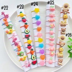 May include: A set of 10 colorful hair ties with various charms, including hearts, fruit, animals, and candy. The hair ties are numbered 22 through 26.