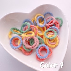May include: A bowl of colorful fuzzy hair ties in blue, green, yellow, and pink. The bowl is heart-shaped and white. The text "Color 7" is written below the bowl.