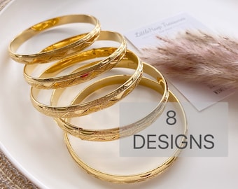 May include: A stack of five gold-toned metal bangles, each featuring a textured surface with a repeating geometric pattern. The bracelets are arranged in a cascading formation. A small card with the text LittleHoop Treasures and 8 DESIGNS is visible.
