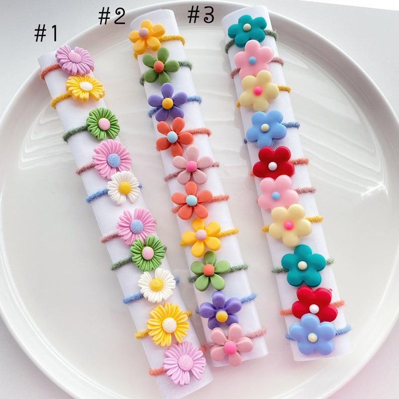 May include: Three rows of colorful flower hair ties with different colored flowers and centers. The hair ties are labeled #1, #2, and #3.