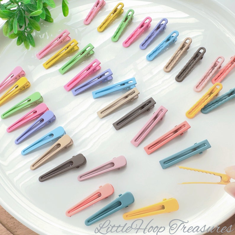 May include: Assortment of colorful plastic hair clips in various pastel shades, including pink, blue, green, yellow, and brown. The clips are arranged on a white surface.  The text "Little Hoop Treasures" is visible in the bottom right corner of the image.