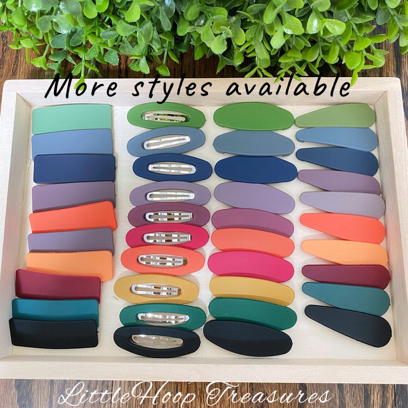 Puede incluir: Una variedad de pinzas para el cabello de colores en diferentes formas y tama&ntilde;os. Las pinzas est&aacute;n dispuestas en una bandeja de madera con el texto "M&aacute;s estilos disponibles" y "Little Hoop Treasures" impreso en la bandeja.