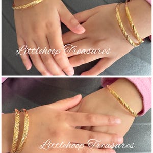May include: Gold-colored bangles with textured designs. The image shows two sets of bangles on a person's hands. The bangles have a repeating pattern and a shiny finish. The text "Littlehoop Treasures" is visible in the image.