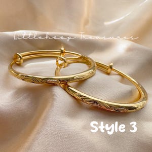 May include: Two gold-colored adjustable bangles with engraved floral patterns. The bangles are displayed on a satin surface. The text "Littlehoop Treasures" and "Style 3" are visible.
