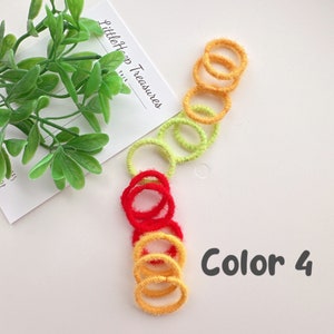 Puede incluir: Un conjunto de gomas para el pelo de colores rojo, amarillo y verde. Las gomas para el pelo est&aacute;n hechas de material peludo y est&aacute;n apiladas. El texto "Color 4" est&aacute; escrito en negro sobre un fondo blanco.