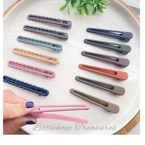Op de afbeelding: Assortiment van 10 kleurrijke plastic haarclips in verschillende tinten blauw, roze, grijs en bruin. De clips hebben allemaal de vorm van een rechthoek met afgeronde hoeken. De clips zijn in twee rijen op een wit oppervlak gerangschikt. De tekst "Littlehoop Treasures" is zichtbaar in de rechterbenedenhoek van de afbeelding.