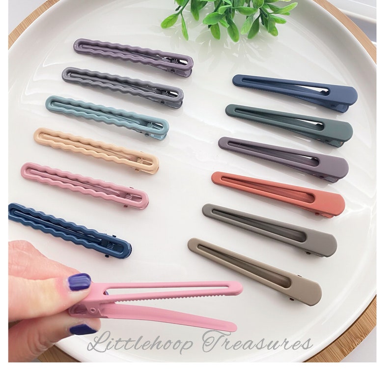 Op de afbeelding: Assortiment van 10 kleurrijke plastic haarclips in verschillende tinten blauw, roze, grijs en bruin. De clips hebben allemaal de vorm van een rechthoek met afgeronde hoeken. De clips zijn in twee rijen op een wit oppervlak gerangschikt. De tekst "Littlehoop Treasures" is zichtbaar in de rechterbenedenhoek van de afbeelding.