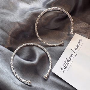 May include: Two silver-toned cuff bracelets featuring a textured, braided-style pattern along the band and rounded ball ends. A white rectangular card is present with the black printed text Littlehoop Treasures USA.