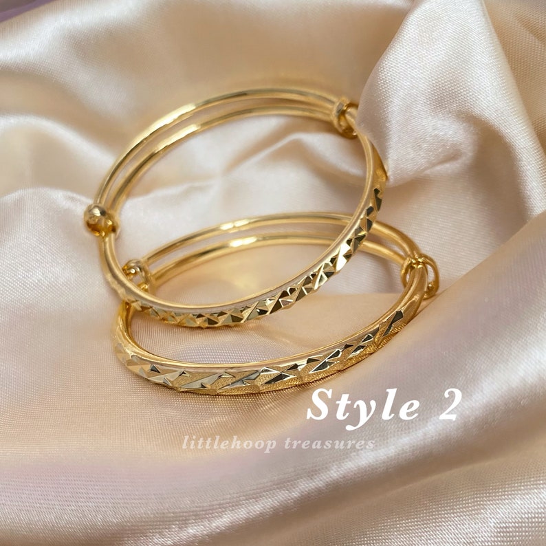 May include: Two gold-colored bangles with a geometric pattern and a smooth, shiny finish. The bangles are displayed on a satin fabric. The text "Style 2" and "littlehoop treasures" are visible.