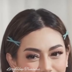 May include: A woman with long brown hair is wearing two light blue hair clips in her hair. The clips are in the shape of a cross.