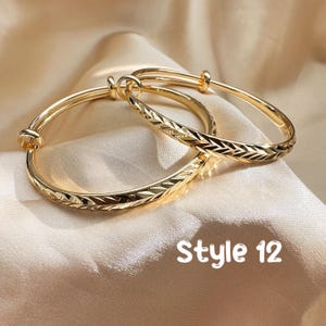 May include: Two gold-colored adjustable bangles with engraved chevron patterns. The bangles are displayed on a satin surface. The text "Style 12" is visible in the image.