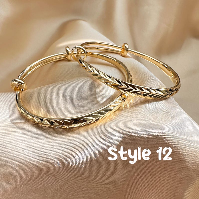 May include: Two gold-colored adjustable bangles with engraved chevron patterns. The bangles are displayed on a satin surface. The text "Style 12" is visible in the image.