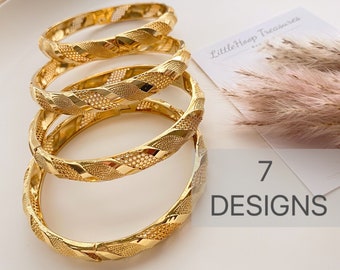 May include: Four gold-toned bangle bracelets with intricate, woven designs. The bracelets are stacked on top of each other. The text "7 DESIGNS" is visible in the image.