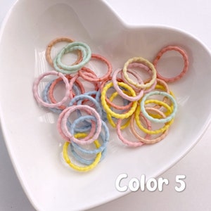 May include: A bowl filled with colorful hair ties in pastel shades of pink, yellow, and blue. The bowl is white and heart-shaped. The text "Color 5" is written at the bottom of the bowl.