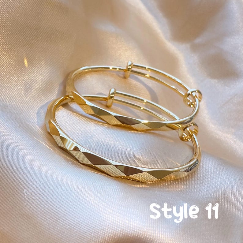 May include: Two gold-colored adjustable bracelets. The bracelets have a geometric diamond pattern on the front and a smooth, rounded design on the sides. The text "Style 11" is visible in white.