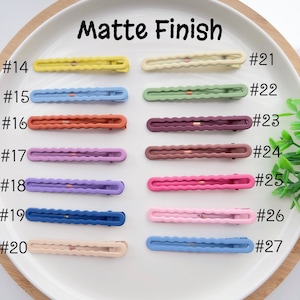 Op de afbeelding: Tien paar matte haarclips in verschillende kleuren, waaronder geel, blauw, groen, bruin, paars, roze en beige. De clips zijn genummerd van 14 tot en met 27.