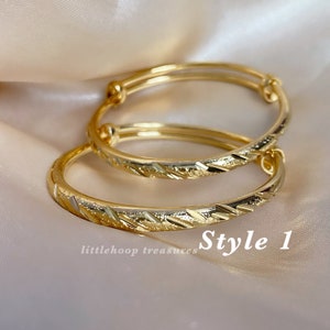 May include: Two gold-colored adjustable bangles with a textured, geometric design. The bangles are labeled "Style 1" and are from "littlehoop treasures". The jewelry is displayed on a soft, neutral background.