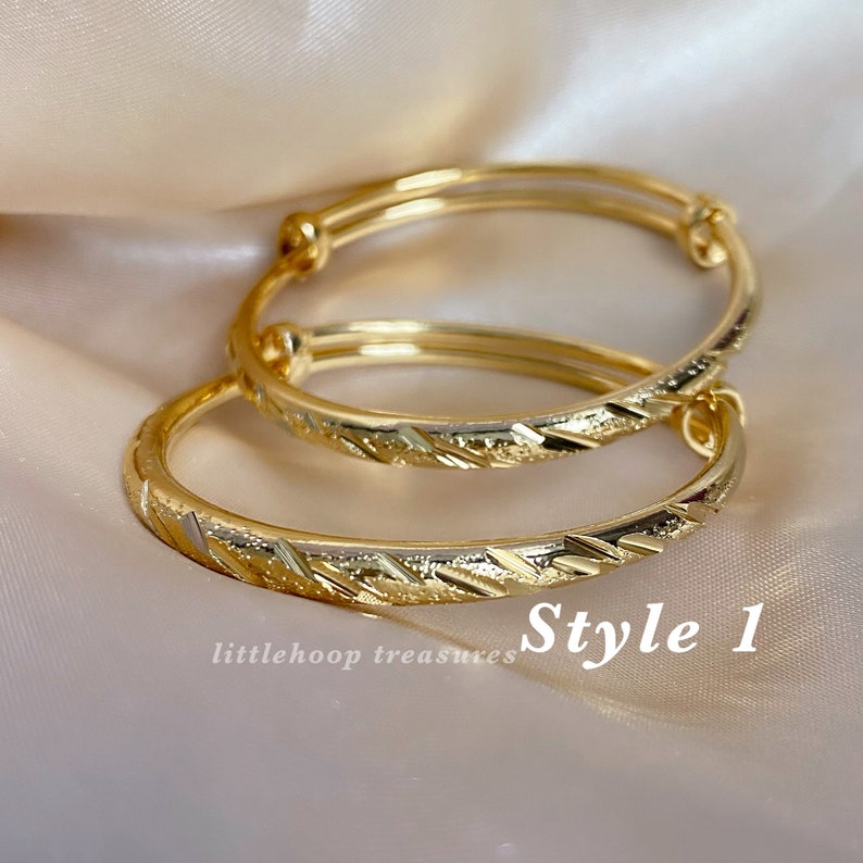 May include: Two gold-colored adjustable bangles with a textured, geometric design. The bangles are labeled "Style 1" and are from "littlehoop treasures". The jewelry is displayed on a soft, neutral background.