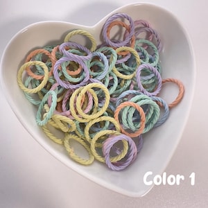 May include: A white heart-shaped bowl filled with a variety of pastel-colored rope rings. The rings are in shades of light blue, light green, light pink, and yellow. The text "Color 1" is written in black at the bottom of the image.
