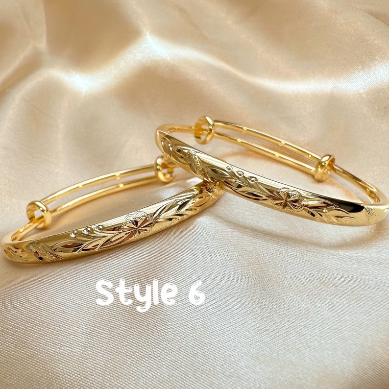 May include: Two gold-colored adjustable bangles with floral and leaf patterns. The bangles are displayed on a satin surface. The text "Style 6" is visible in the image.