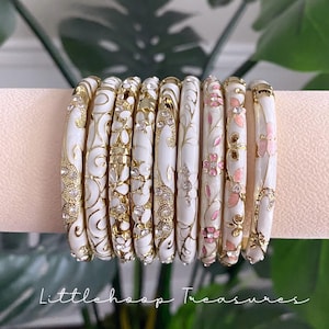 Op de afbeelding: Een set van negen witte emaille armbanden met goudkleurige filigraanpatronen en ingebedde heldere kristallen. Sommige armbanden hebben roze bloemaccenten. De tekst Littlehoop Treasures staat in het wit onderaan de afbeelding.