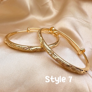 May include: Two gold-colored adjustable bangles with a starburst pattern. The bangles are displayed on a satin surface. The text "Style 7" is visible at the bottom of the image. Jewelry.