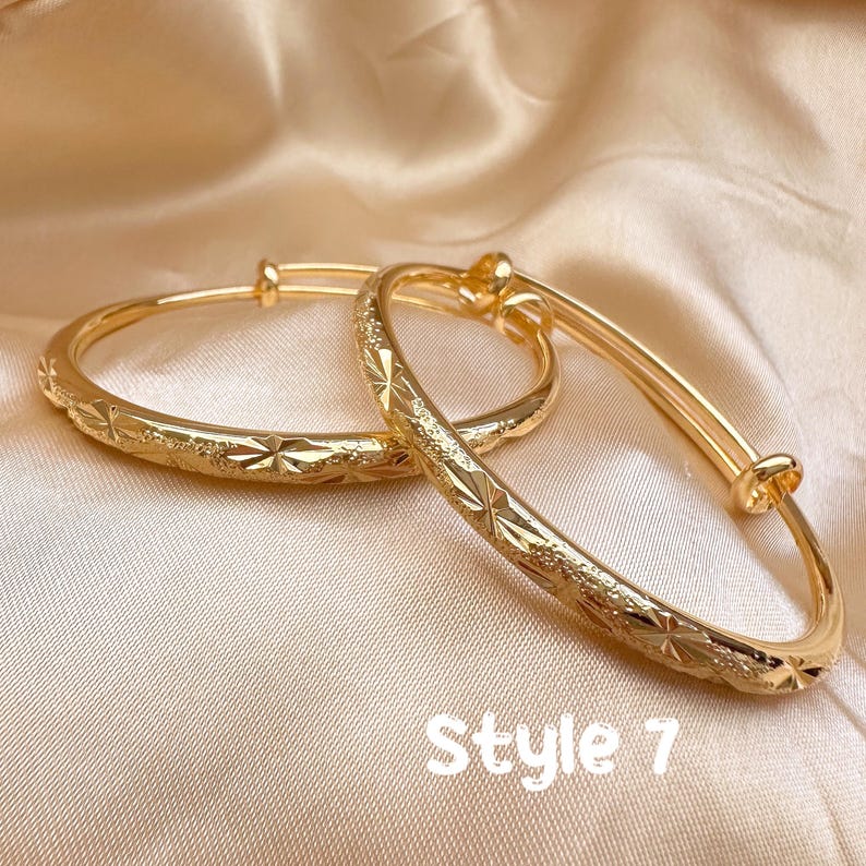 May include: Two gold-colored adjustable bangles with a starburst pattern. The bangles are displayed on a satin surface. The text "Style 7" is visible at the bottom of the image. Jewelry.