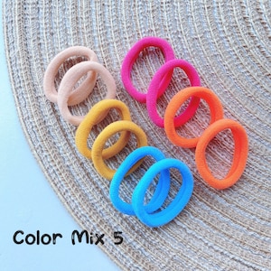 May include: A set of 10 colorful hair ties in a rainbow of colors, including pink, orange, yellow, blue, and peach. The hair ties are arranged in a circle on a woven surface. The text "Color Mix 5" is visible in the image.