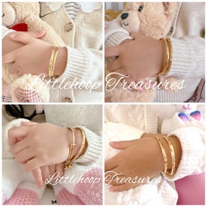 May include: Four images showcasing gold-colored bracelets on a child's wrist. The bracelets have engraved patterns and are worn with a cream-colored sweater. The text "Littlehoop Treasures" is visible in the images.