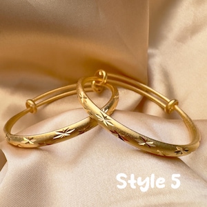 May include: Two gold-colored adjustable bangles with starburst patterns. The bangles are displayed on a satin-like fabric. The text "Style 5" is visible in the image.