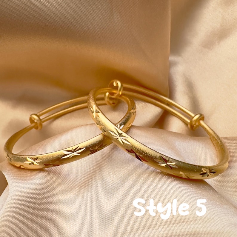 May include: Two gold-colored adjustable bangles with starburst patterns. The bangles are displayed on a satin-like fabric. The text "Style 5" is visible in the image.